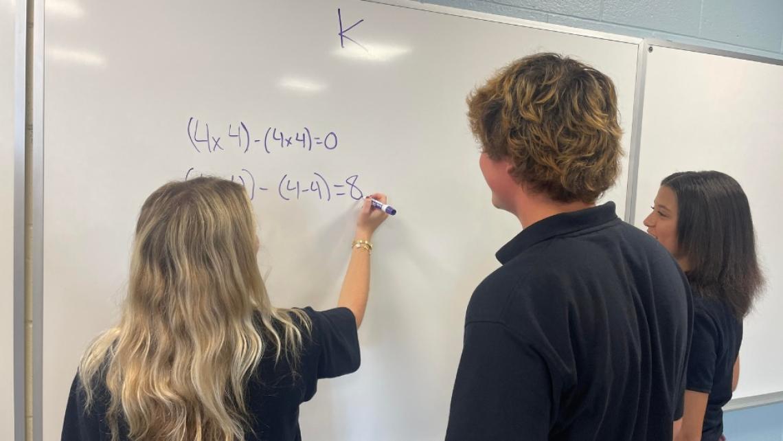 3 students working on a math problem at a whiteboard