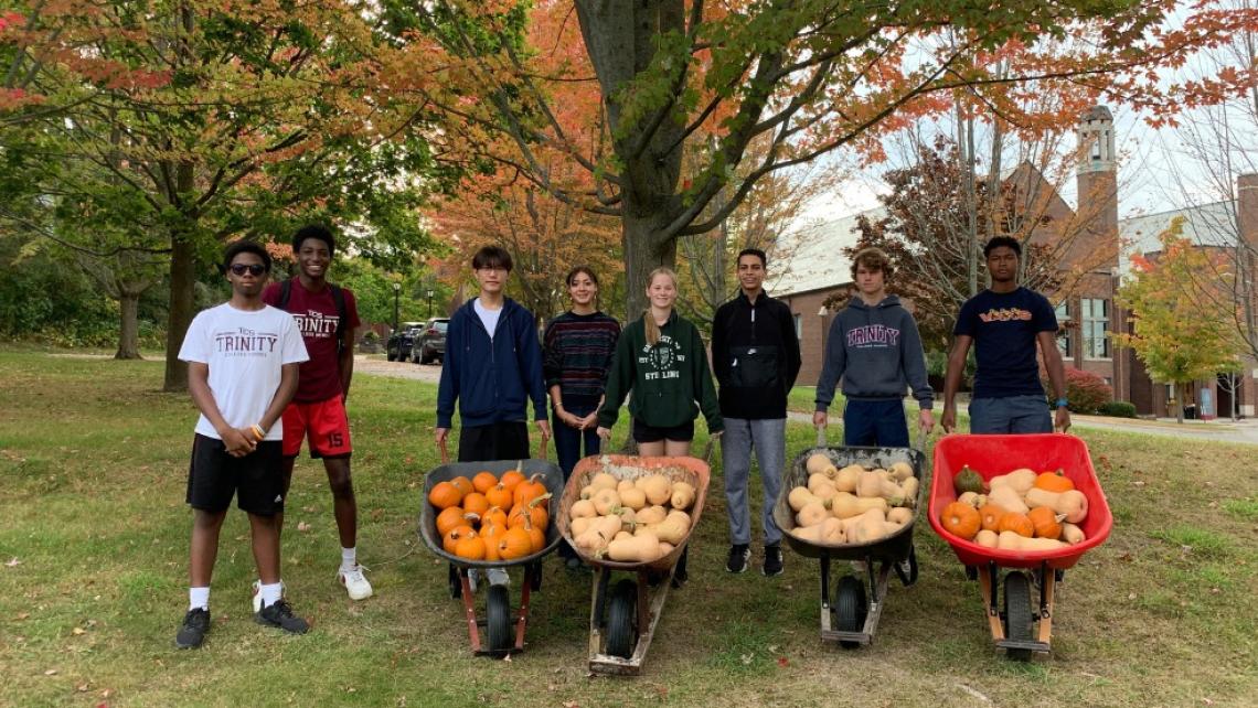 Students holding wheelbarrows filled with pumpkins and butternut squash