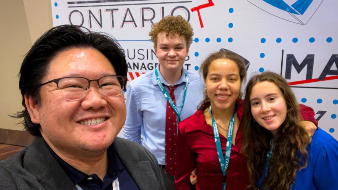 Teacher and three students in front of a DECA Ontario backdrop