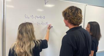 3 students working on a math problem at a whiteboard