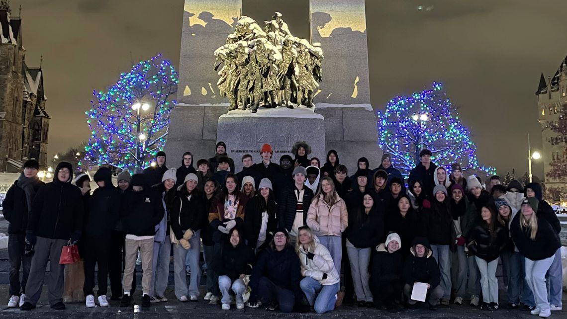Group of students standing in front of the National War Memorial in Ottawa at nighttime, with the monument lit by spotlights