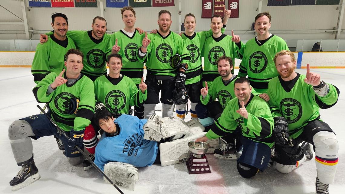 Group oHockey team in green jerseys, posed on the ice with trophy, raising index fingers in number one gesture