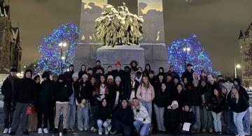 Group of students standing in front of the National War Memorial in Ottawa at nighttime, with the monument lit by spotlights